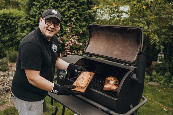 Mann bereitet Lachs auf Grill zu, umgeben von grünem Garten
