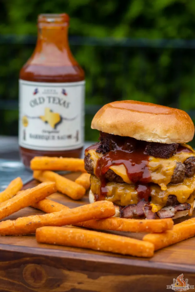 Burger mit Old Texas BBQ Sauce und Pommes auf Holzbrett im Freien