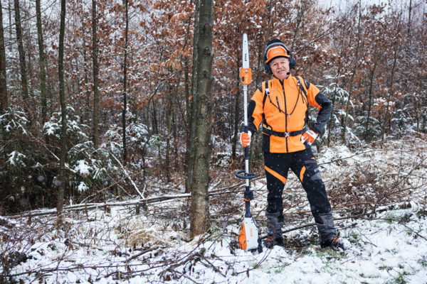 Forstarbeiter in STIHL Schutzausrüstung mit Motorsäge im verschneiten Wald
