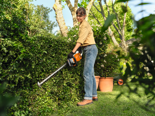 Frau benutzt STIHL Akku-Heckenschere in einem blühenden Garten