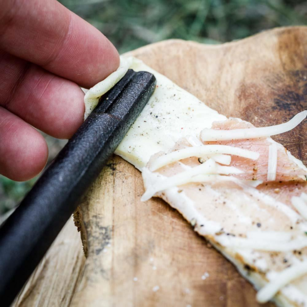 Hand wickelt Teig mit Schinken und Käse auf Petromax Stockbrot Spieß