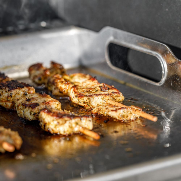 Marinierte Hähnchenspieße auf einer Edelstahl-Grillplatte mit Auffangrinne und Henkeln