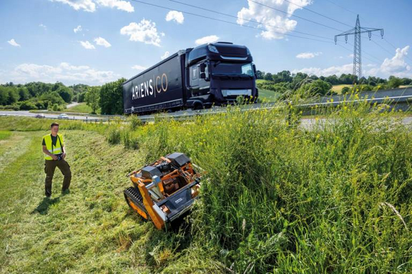 Mann bedient ferngesteuerten Schlegelmäher AS 1000 Ovis RC auf steiler Böschung neben Autobahn