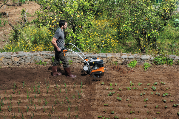 Mann verwendet STIHL MH 685 Motorhacke in einem Garten mit Obstbäumen