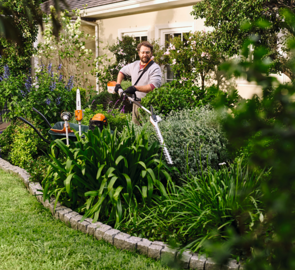 Mann verwendet STIHL KMA 80 R in einem blühenden Garten