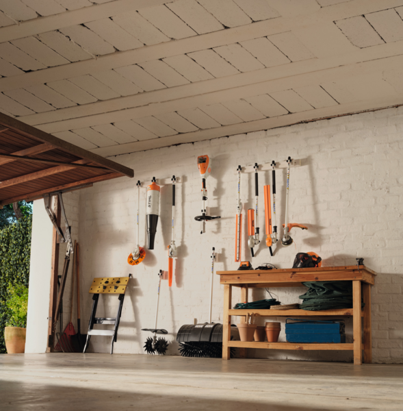 Organisierte Werkstatt mit STIHL Gartenwerkzeugen an weißer Wand und Holztisch