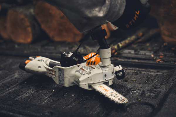 STIHL GTA 40 Akku-Motorsäge auf feuchtem Untergrund mit Holzstämmen im Hintergrund