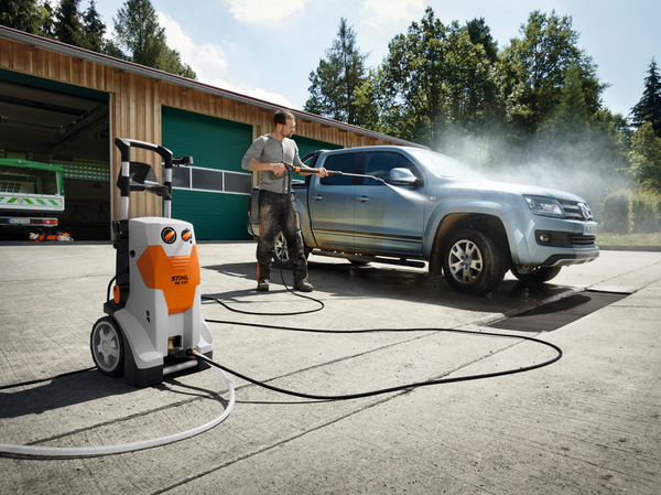 Mann reinigt Pickup mit STIHL Hochdruckreiniger vor grüner Werkstatt