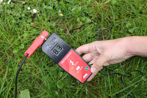 Person misst Spannung mit AKO Digital Voltmeter auf grüner Wiese