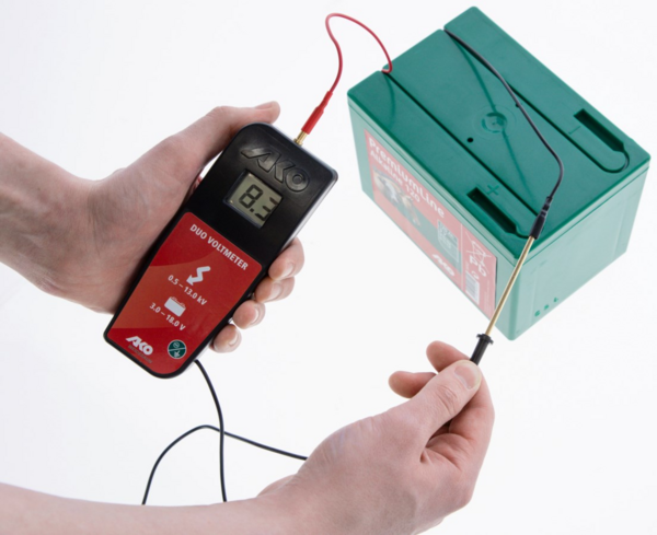 Hand hält AKO DUO-Voltmeter angeschlossen an grüne Batterie