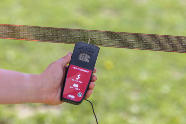Hand hält AKO DUO-Voltmeter zur Messung der Spannung eines Elektrozauns im Freien