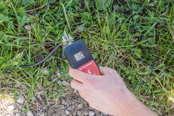 Hand hält AKO DUO-Voltmeter zur Spannungsmessung an einem Weidezaun in natürlicher Umgebung