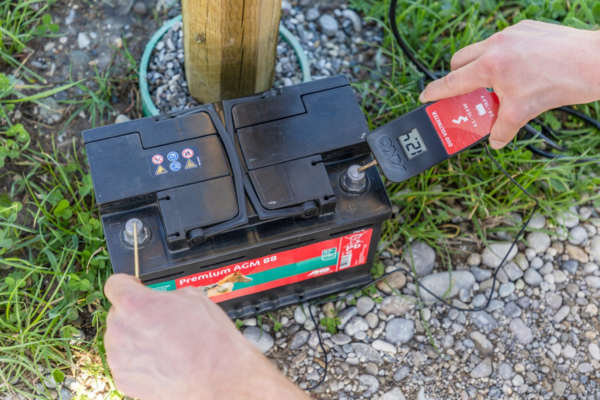 Person misst Batteriespannung mit AKO Digital Voltmeter im Freien
