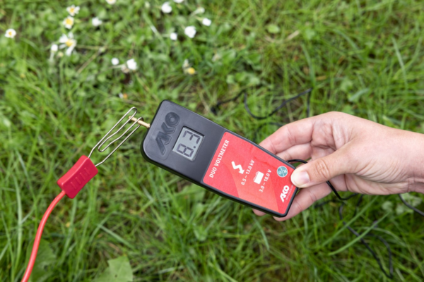 Hand hält AKO DUO-Voltmeter im Gras zur Spannungsmessung
