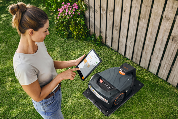 Frau bedient STIHL iMOW 7 EVO Mähroboter mit Tablet im Garten