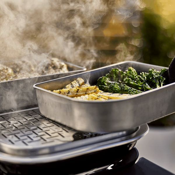 Elektrogrill mit Edelstahlschalen dampfendem Fisch und Gemüse im Freien