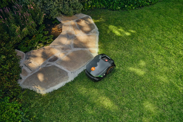 STIHL iMOW 3 EVO Mähroboter mäht Rasen neben steinernem Weg und Teich