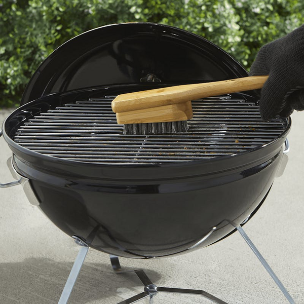 Person reinigt Grillrost mit Weber Grillbürste auf schwarzem Kugelgrill
