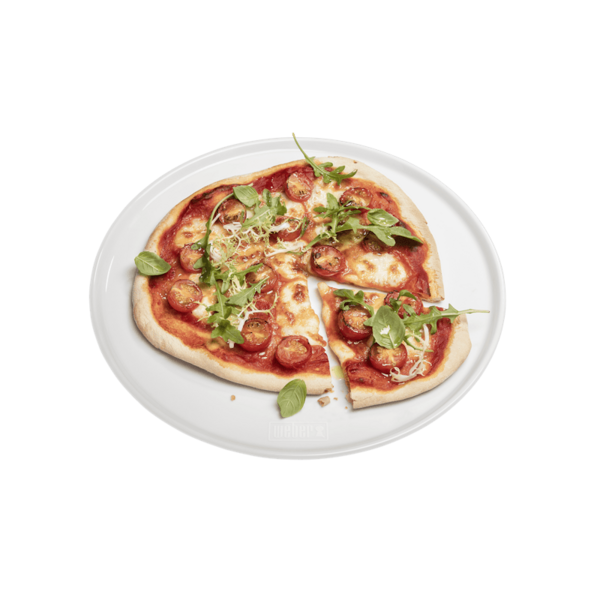 Frische Pizza auf Weber Porzellan-Pizzateller vor grünem Hintergrund