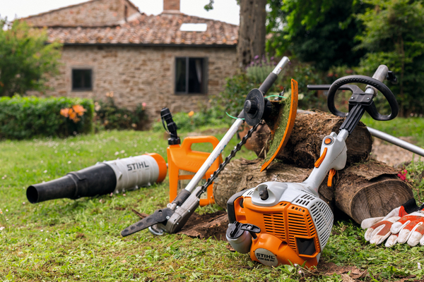 STIHL Gartengeräte inklusive KM 56 RC-E KombiMotor und Aufsätze auf Rasen vor Steinhaus
