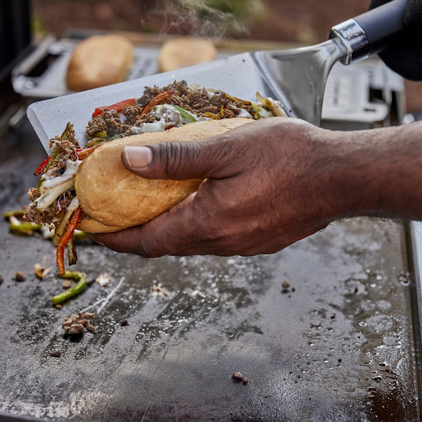 Hand benutzt Weber Planchawender um gegrilltes Gemüse und Fleisch in Brötchen zu geben