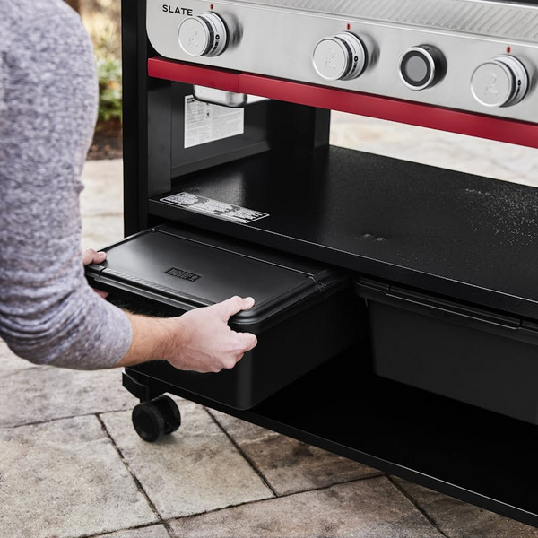Person zieht schwarze Weber Works Aufbewahrungsbox unter einem Grilltisch hervor