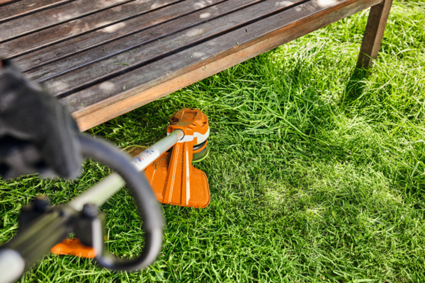 STIHL FSA 70 R Akku-Motorsense im Einsatz im Garten neben Holzmöbel