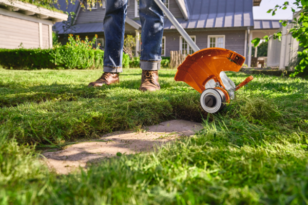 Person verwendet STIHL FSA 50 Akku-Motorsense im sonnigen Garten