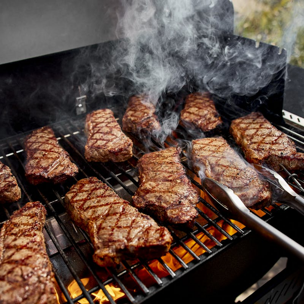 Steaks mit Grillstreifen auf Weber SEARWOOD Holzpelletgrill mit sichtbaren Flammen und aufsteigendem Rauch