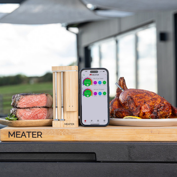 Smartes Fleischthermometer MEATER Pro Duo neben Steak und gebratenem Hähnchen in Außenküche