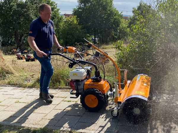 Mann bedient AS 600 MultiPro Mäher mit Honda Motor auf gepflastertem Weg