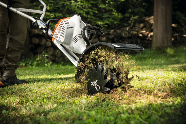 Stihl RL-MM Rasenlüfter in Aktion auf einem grünen Rasen mit aufgewirbeltem Gras und Erde