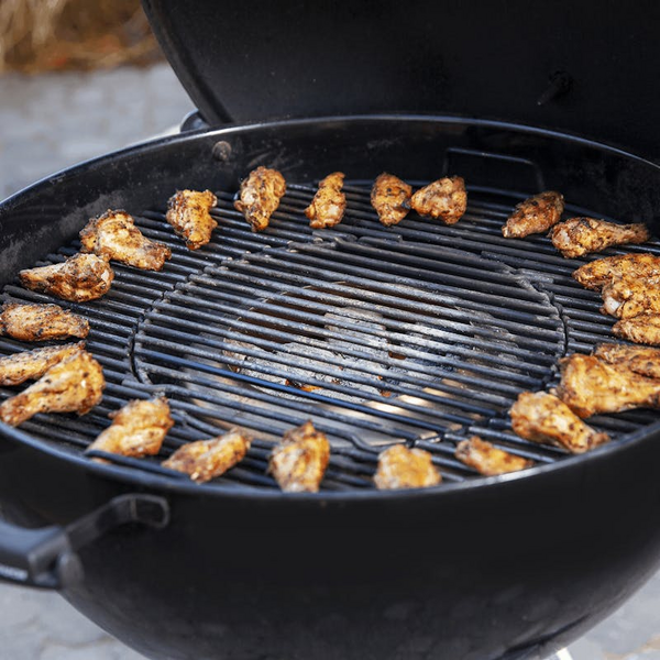 Geöffneter schwarzer Kugelgrill mit knusprig gegrillten Hähnchenflügeln auf einem Grillrost