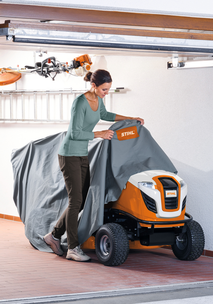 Frau zieht STIHL Abdeckhaube über einen Aufsitzmäher in einer Garage