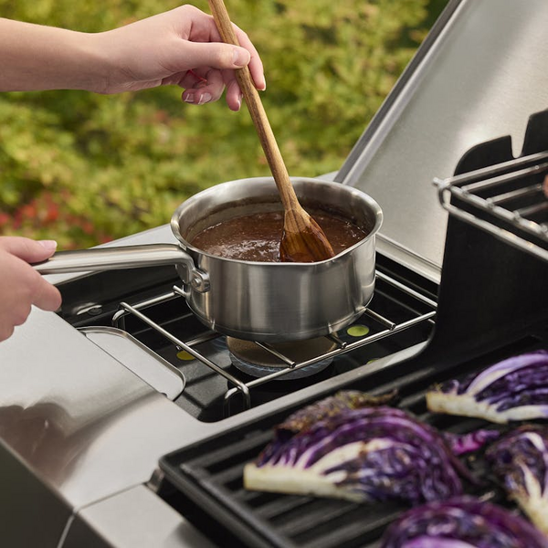 Person verwendet Seitenbrenner eines Weber Gasgrills zum Kochen