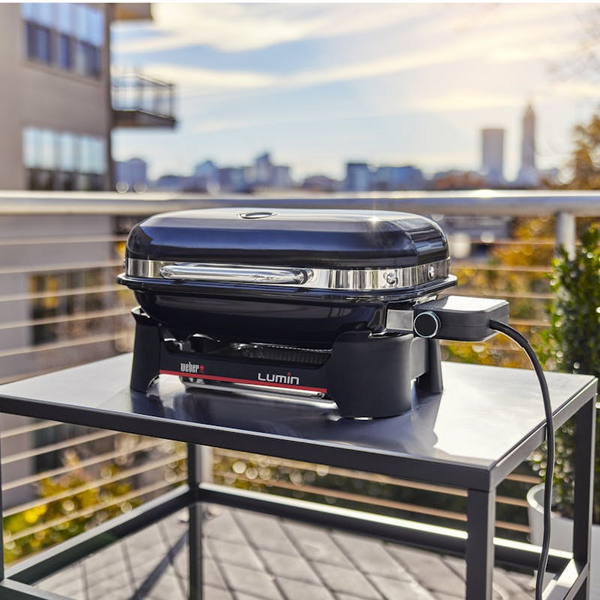 Weber LUMIN COMPACT Elektrogrill auf Terrasse mit städtischer Skyline im Hintergrund