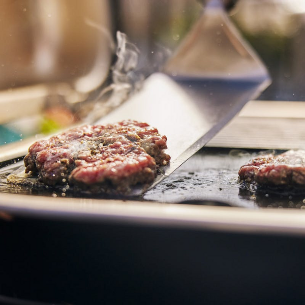 Rinderhacksteaks auf einem Elektrogrill mit sichtbarem Dampf und einem Spatel