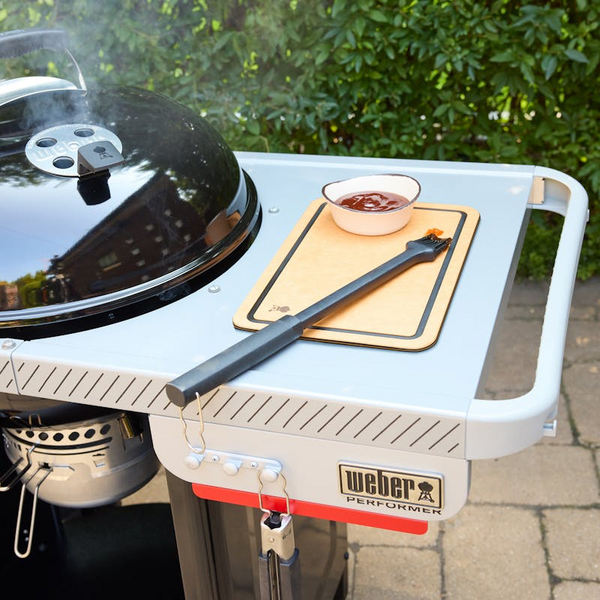 Weber Performer Holzkohlegrill auf Rollwagen mit Seitentisch und Grillzubehör im Freien