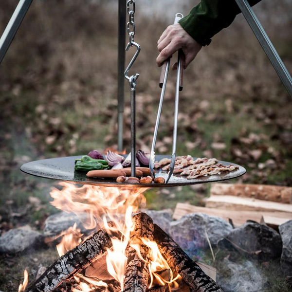 Person verwendet Edelstahl Grillzange am offenen Feuer mit Gemüse und Würstchen auf Grillrost
