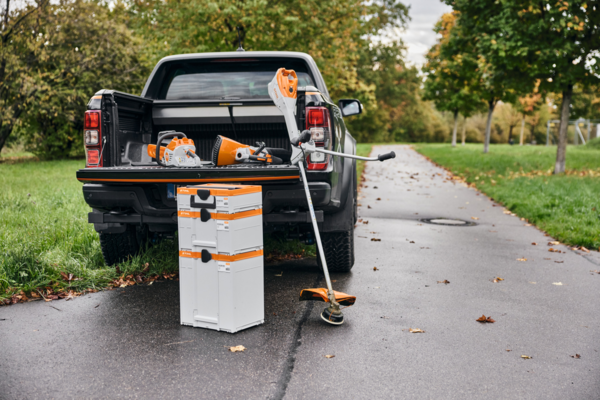 STIHL Akku-Box auf Straße neben Pickup-Truck mit Gartenwerkzeugen