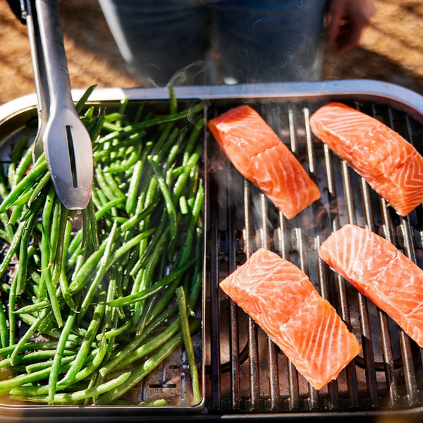 Person grillt Lachs und grüne Bohnen auf einem Elektrogrill im Freien