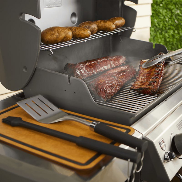 Weber Premium Grillbesteck auf einem Gasgrill mit Steaks und Rippchen im Freien