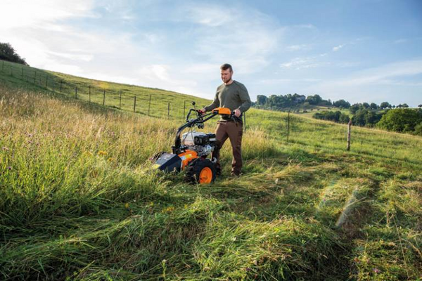 Mann bedient AS LOSI Mähbalken in hügeliger Landschaft