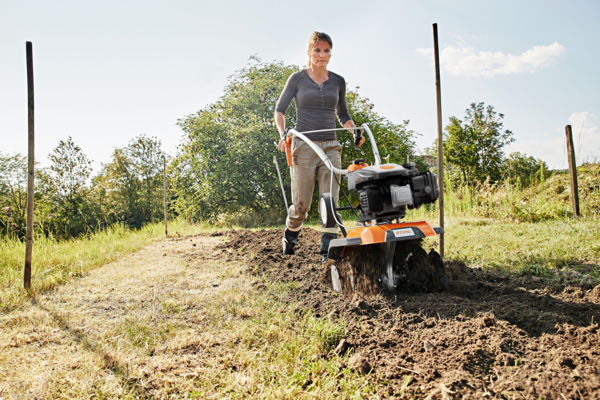 Frau benutzt STIHL MH 445 Motorhacke im Garten bei sonnigem Wetter