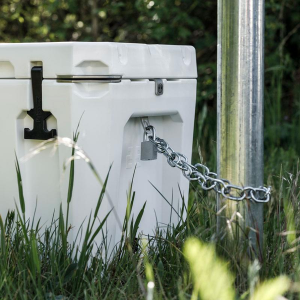 Weiße Petromax Kühlbox gesichert mit Schloss und Kette an Metallpfosten im Grünen