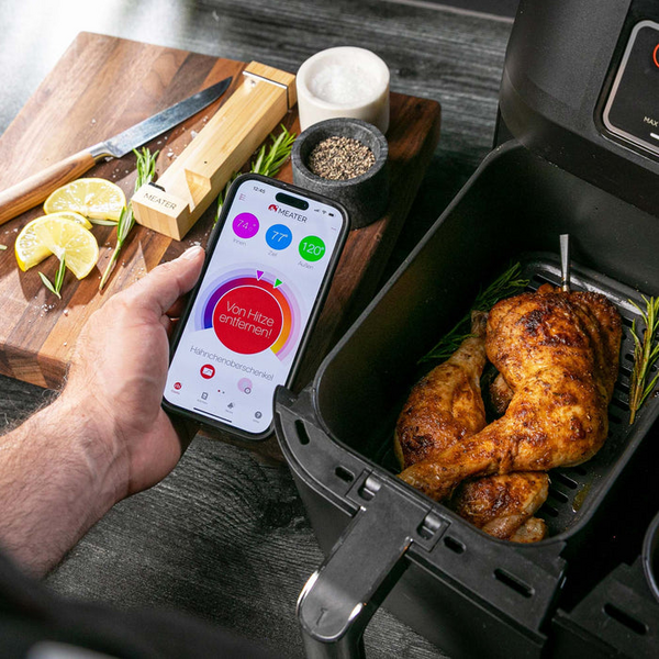 Smartphone mit MEATER App zeigt Garzustand von Hähnchen in moderner Küche