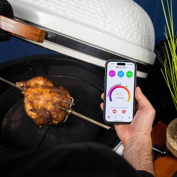 Person verwendet MEATER Pro App neben garendem Hähnchen im Ofen