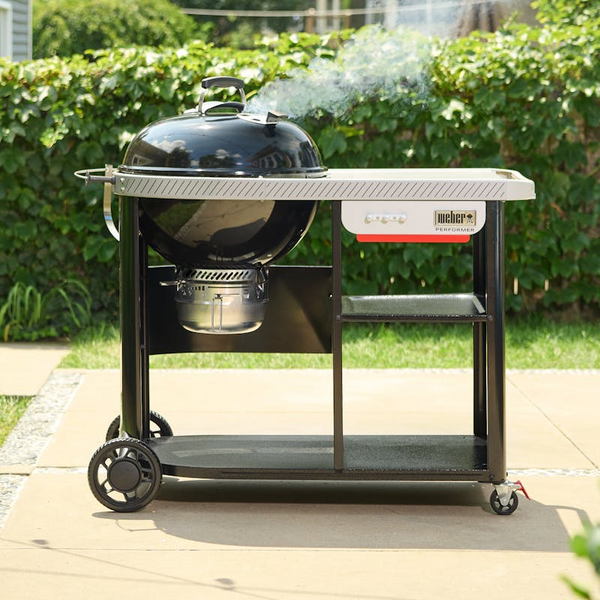 Weber Performer Premium Holzkohlegrill auf Rollwagen mit Rauch und Gartenhintergrund