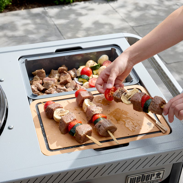 Person preparing kebabs on Weber Performer Premium charcoal grill with side table