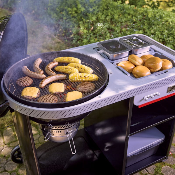Weber Performer Premium Holzkohlegrill mit Essen auf Rost und Seitentisch in einem Garten